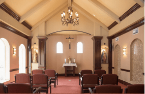 A serene chapel interior with an altar, wooden chairs, and a chandelier.