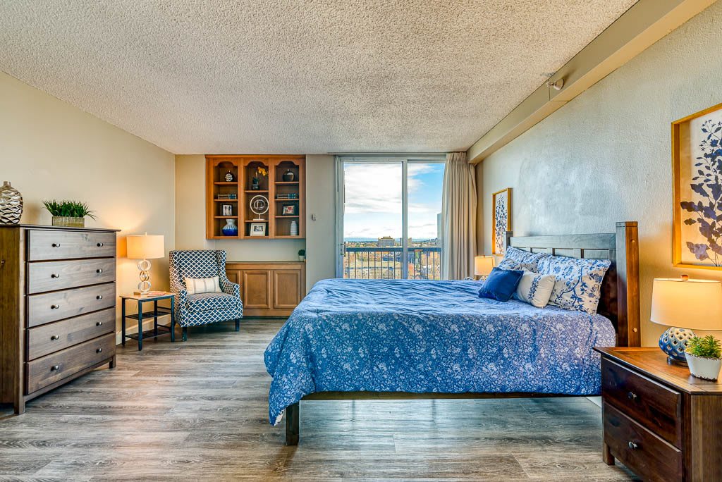 A spacious bedroom with a large bed, wooden flooring, and an armchair by the window.