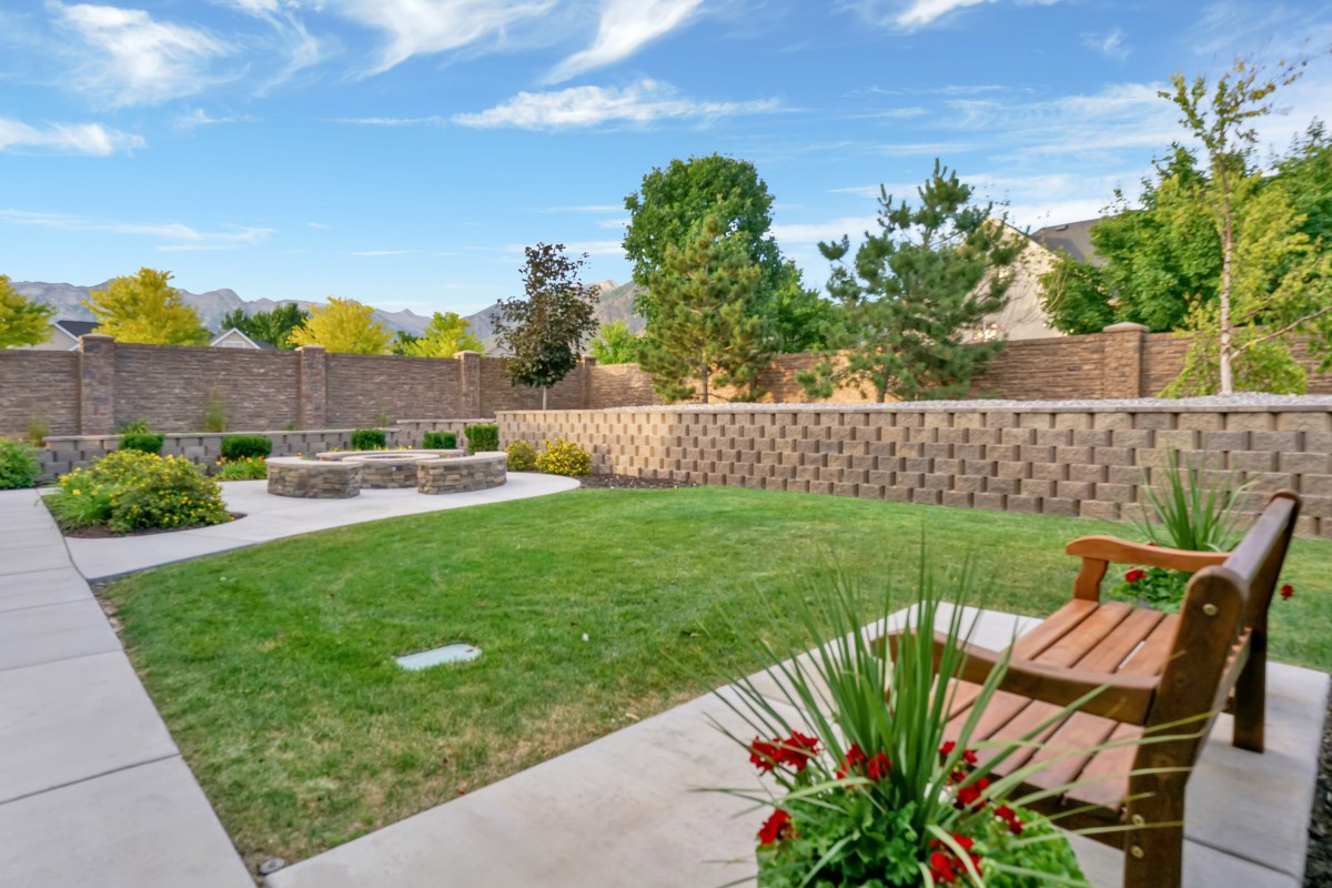 A well-maintained backyard with a grassy area, patio, and outdoor seating surrounded by a brick fence and various plants.