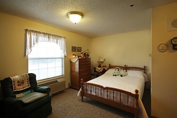 A cozy bedroom with a wooden bed, dresser, and a large window.
