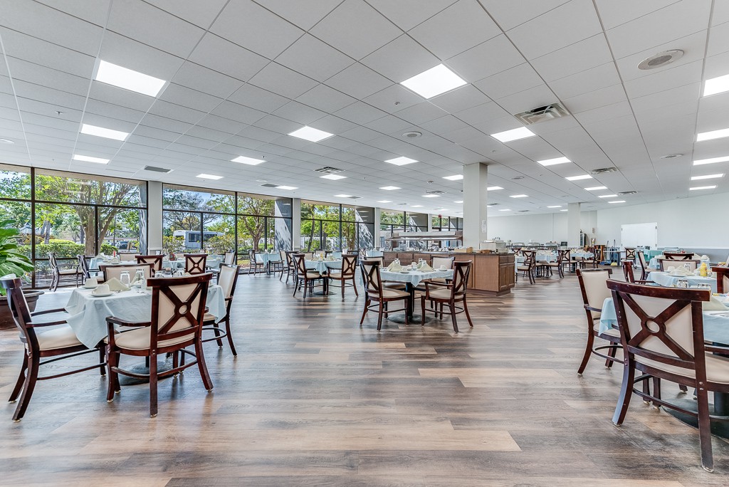 A modern dining area with wooden floors, empty tables and chairs, and large windows.