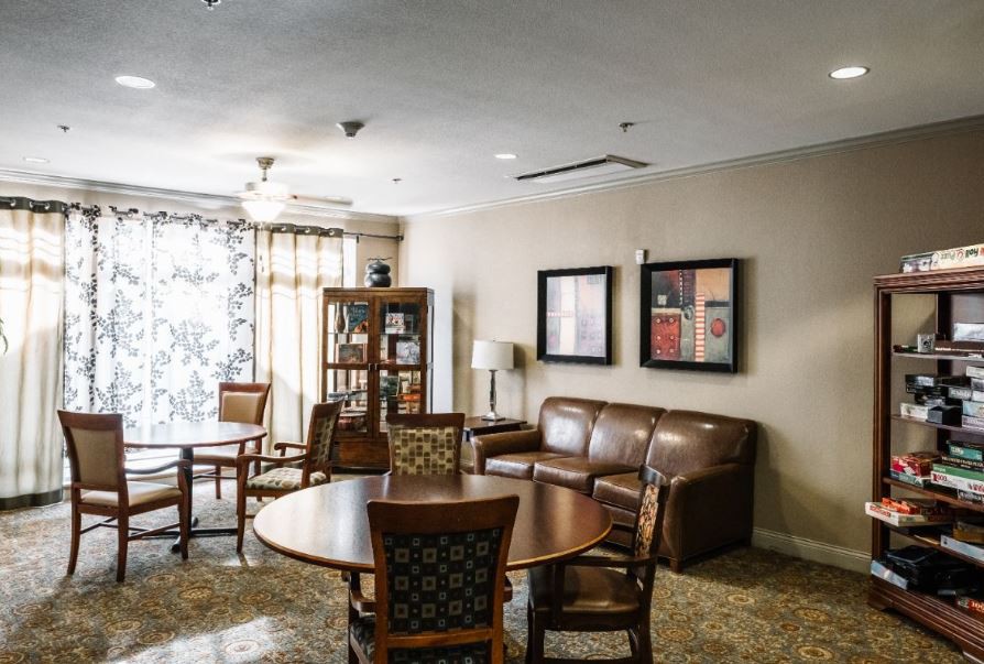 A cozy living room with a sofa, chairs, coffee table, and bookshelf adorned with artwork on the walls.
