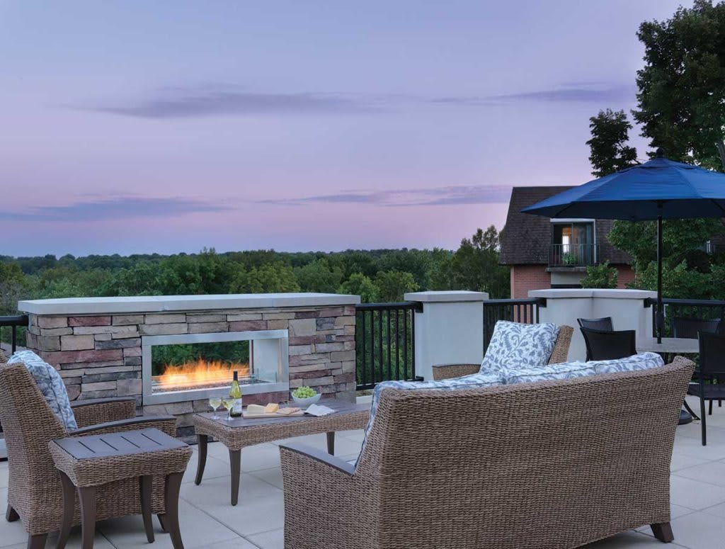 An inviting outdoor patio with a cozy fireplace and comfortable seating, set against a serene evening sky.