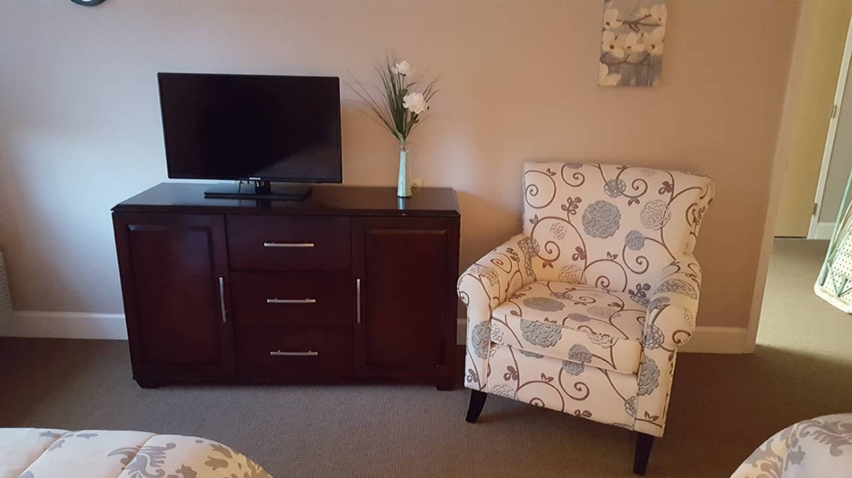A cozy living room corner with a TV on a dark wooden cabinet and a patterned armchair.