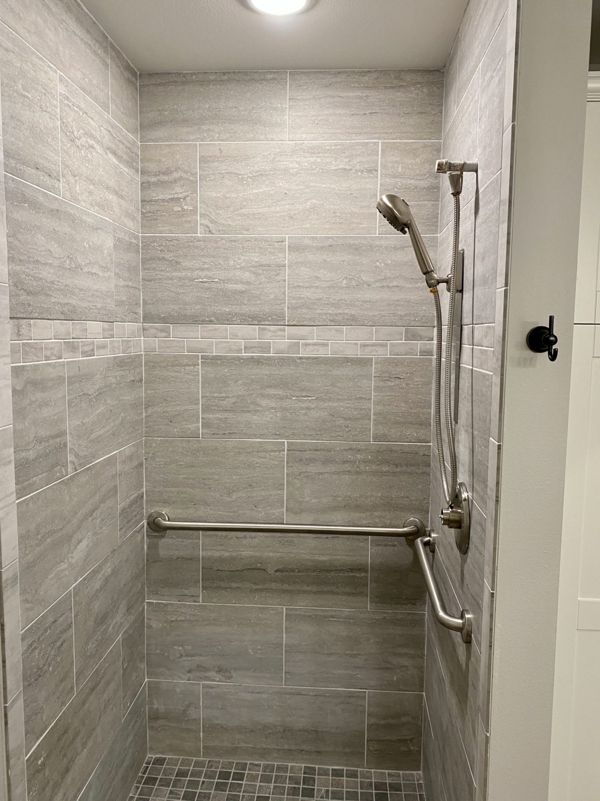 A tiled shower with a handheld showerhead and a grab bar.