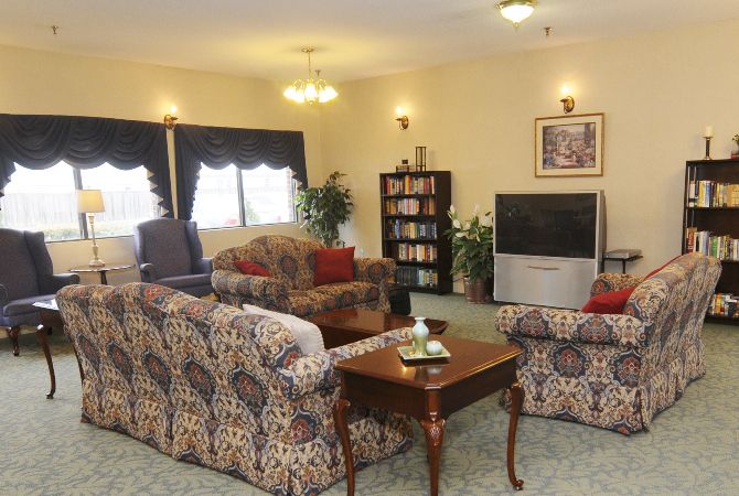 A cozy living room with patterned sofas, a wooden coffee table, and a television near a bookshelf beneath soft lighting.