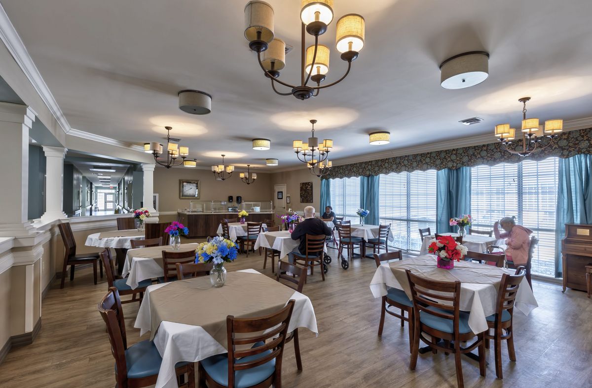 A well-lit dining area with neatly arranged tables and chairs, adorned with chandeliers and decorative table settings.