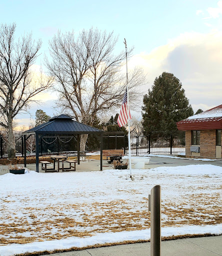 A winter scene featuring a gazebo in a park, surrounded by snow and trees, with an American flag standing tall.