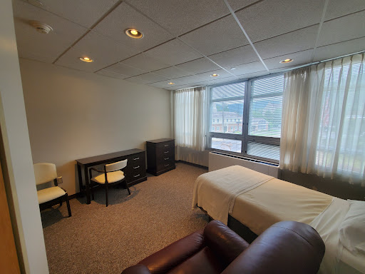 A spacious room featuring a bed, desk, and comfortable seating with large windows providing natural light.