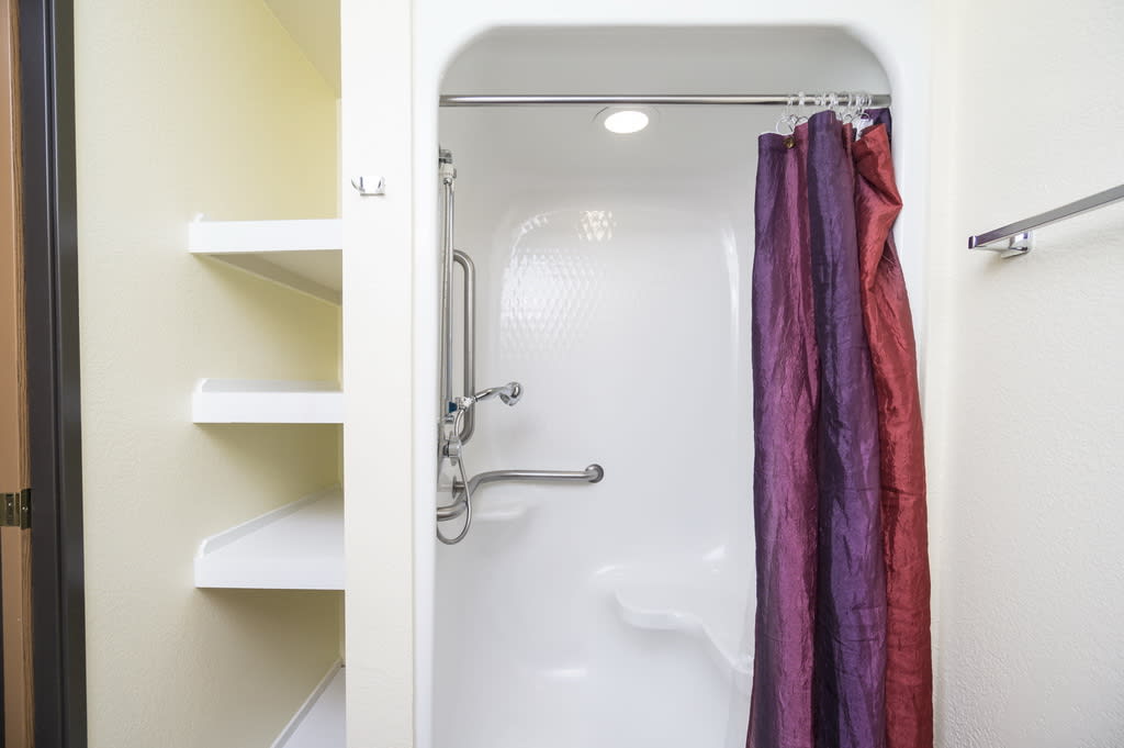 A bathroom featuring a shower with a colorful curtain and adjacent shelves.