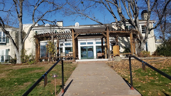 A sunny day at the entrance of a building with a pathway leading to it, flanked by trees.