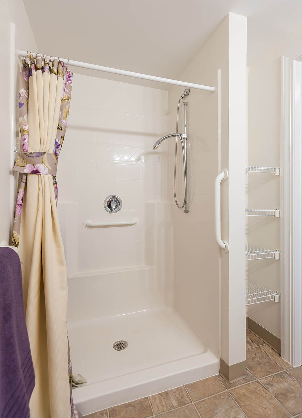 A clean and simple walk-in shower with a floral curtain and grab bar.