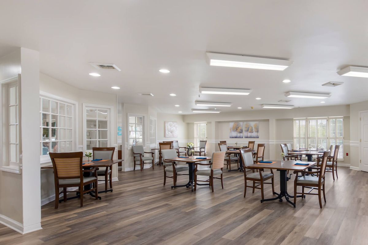 A spacious and modern dining room with multiple tables and chairs, illuminated by bright lighting.