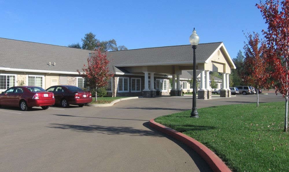 A view of a building with a driveway, parked car, and surrounding greenery.