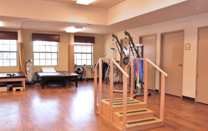 A spacious rehabilitation room equipped with exercise equipment and wooden stairs for therapy exercises.
