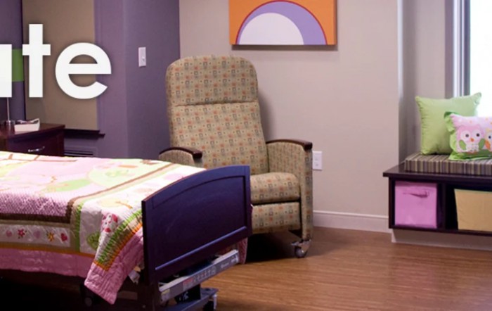 A hospital room featuring a comfortable recliner chair and a bed with colorful blankets.