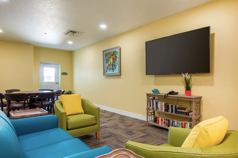 A cozy living room with vibrant furniture, a large TV, and a filled bookshelf.