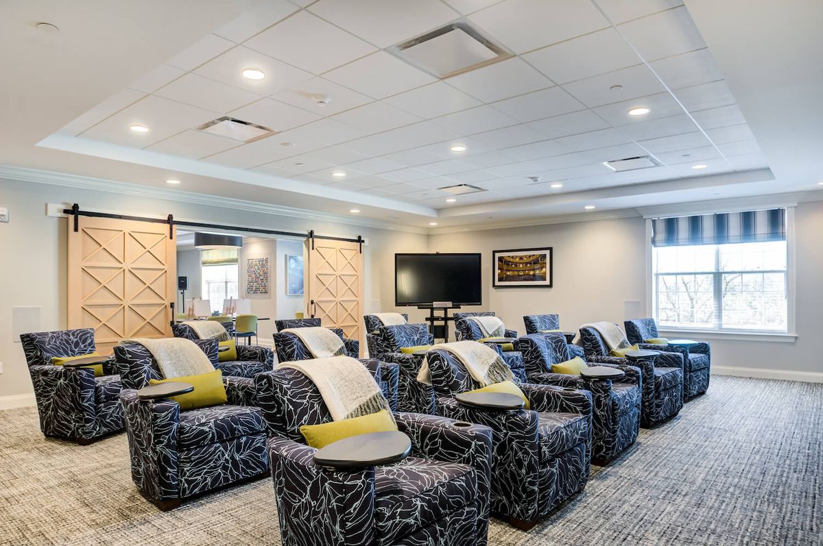 A modern theater room featuring rows of patterned recliner chairs with small individual tables, all facing a large screen.