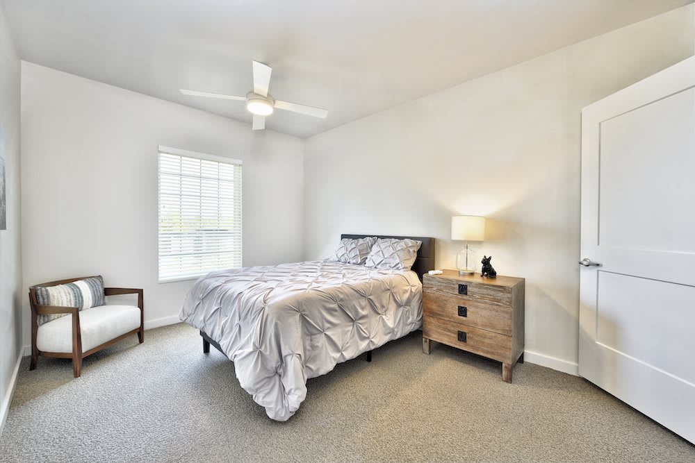 A simple, modern bedroom with a bed, nightstand, and ceiling fan.