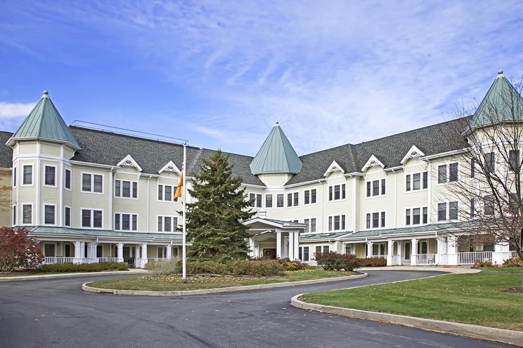 A large residential building with a pointed roof and surrounding greenery on a clear day.