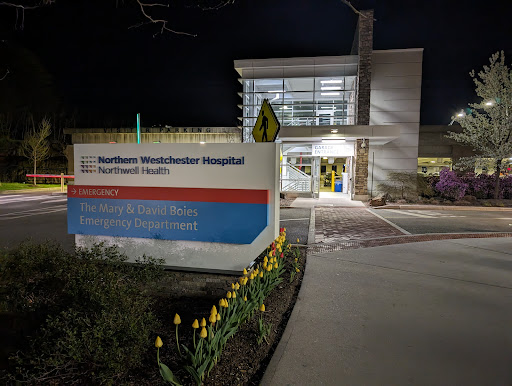 A view of the hospital entrance at night, showcasing modern architecture and illuminated signage.