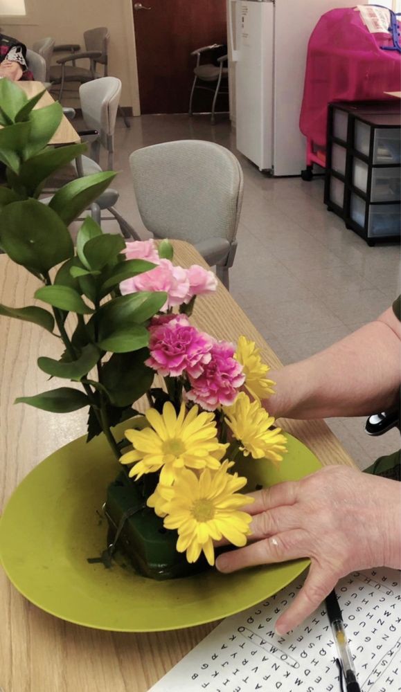 A person arranging a bouquet of yellow daisies and pink carnations on a table.