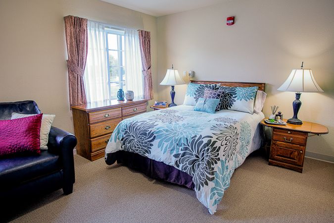 A cozy bedroom with a neatly made bed, wooden furniture, and a window with curtains.