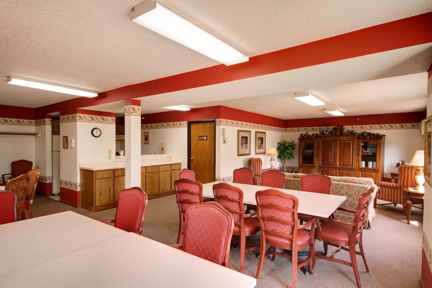 A spacious meeting room with red chairs and white tables, decorated with paintings and plants.