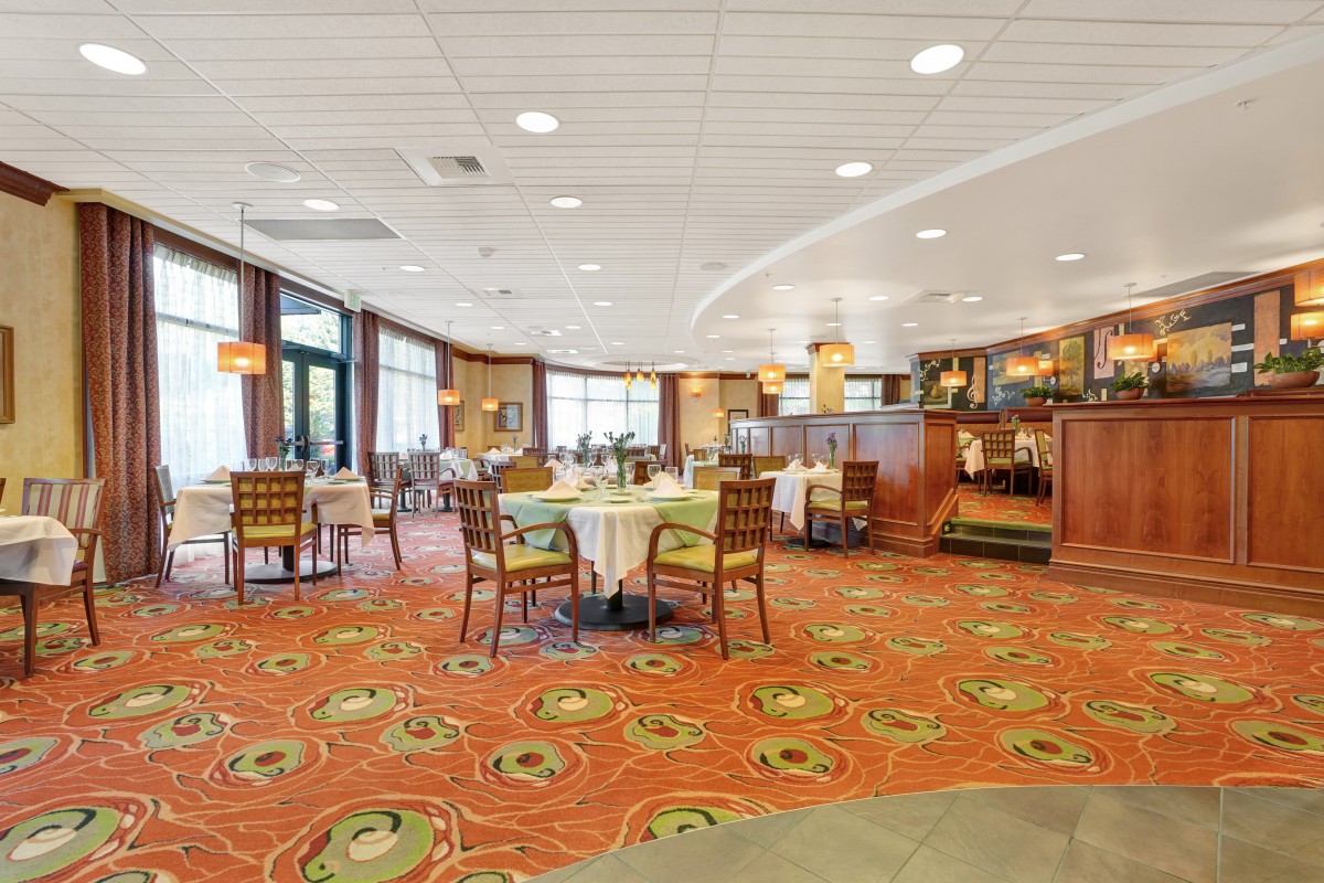 A spacious restaurant interior with neatly arranged tables and chairs on a patterned carpet.