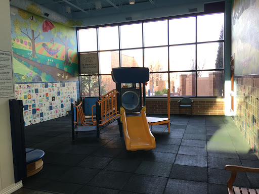 A bright and inviting indoor playground featuring a slide and play equipment, surrounded by large windows.