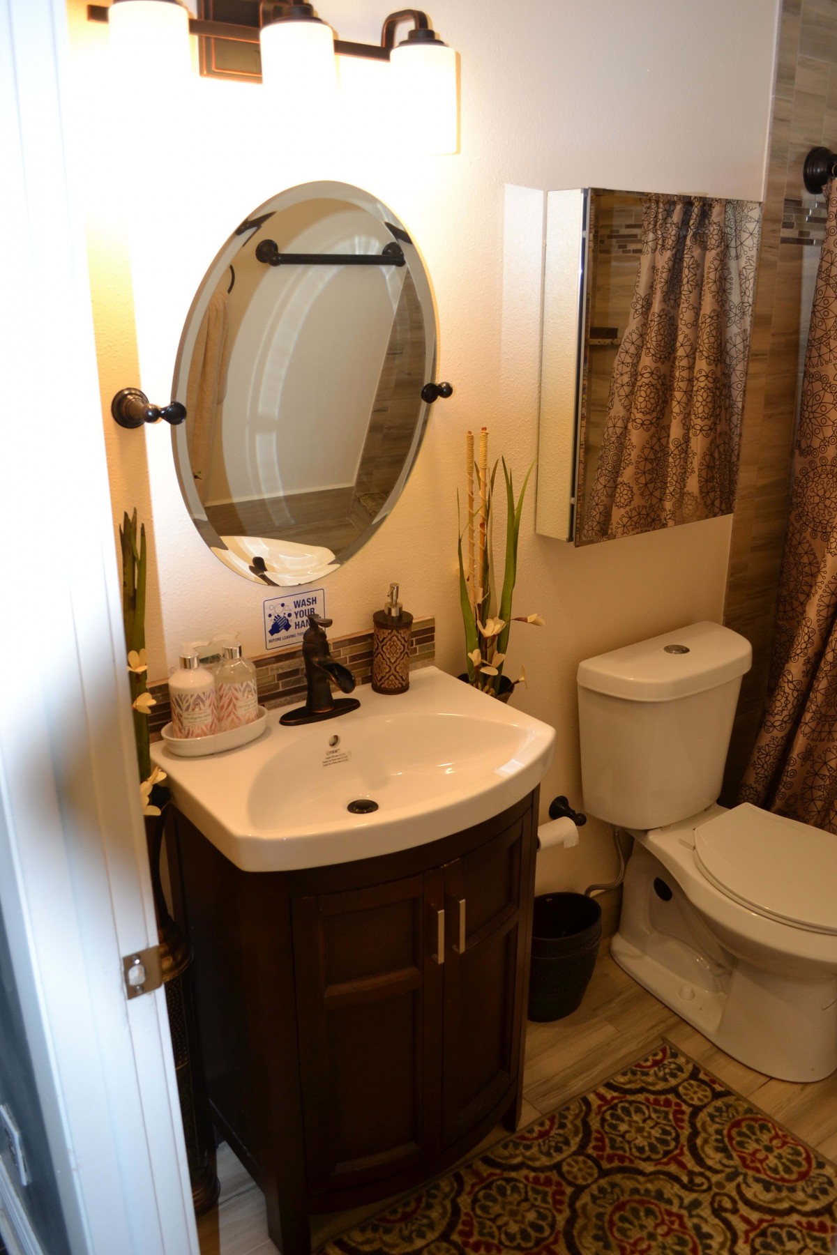 A cozy bathroom with a sink and mirror, featuring a toilet and decorative elements.