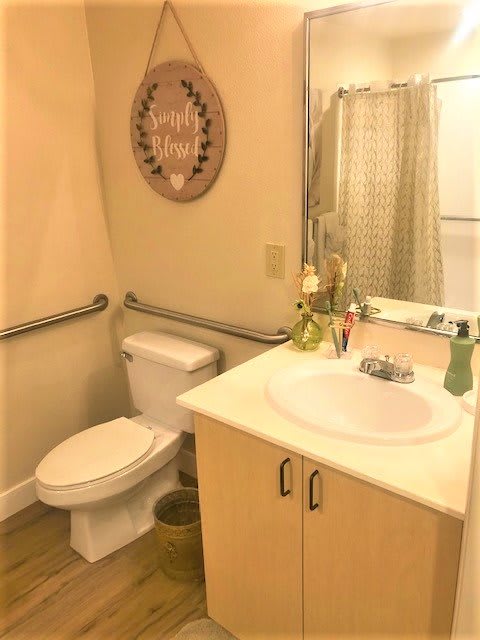 A clean and well-lit bathroom featuring a toilet, sink, mirror, and shower with a decorative wall piece.