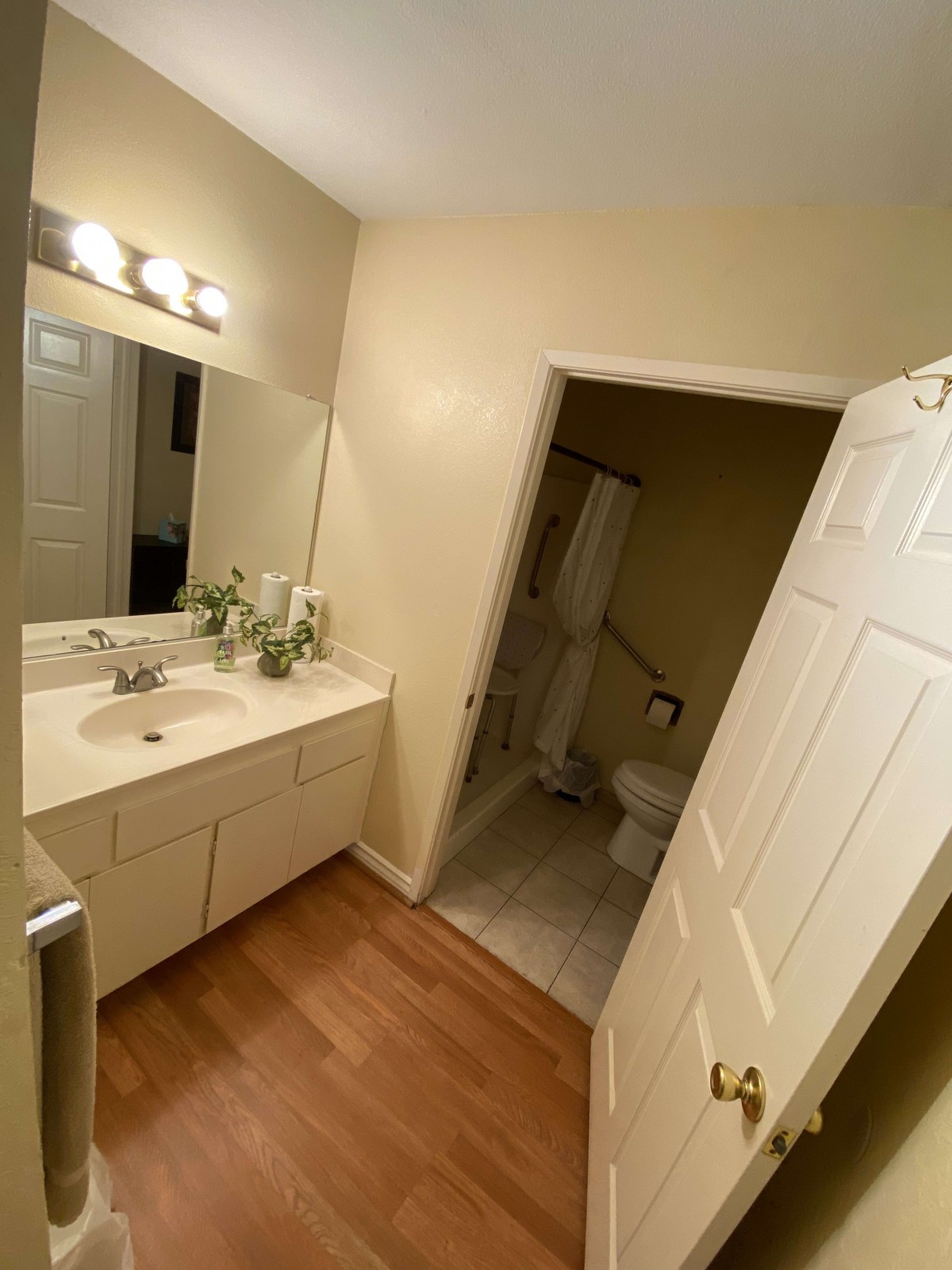A well-lit bathroom with a sink, large mirror, and adjacent toilet.