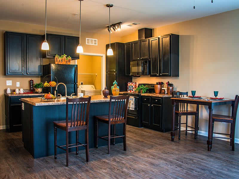 A modern kitchen with black cabinets and a central island, featuring pendant lighting and bar stools.
