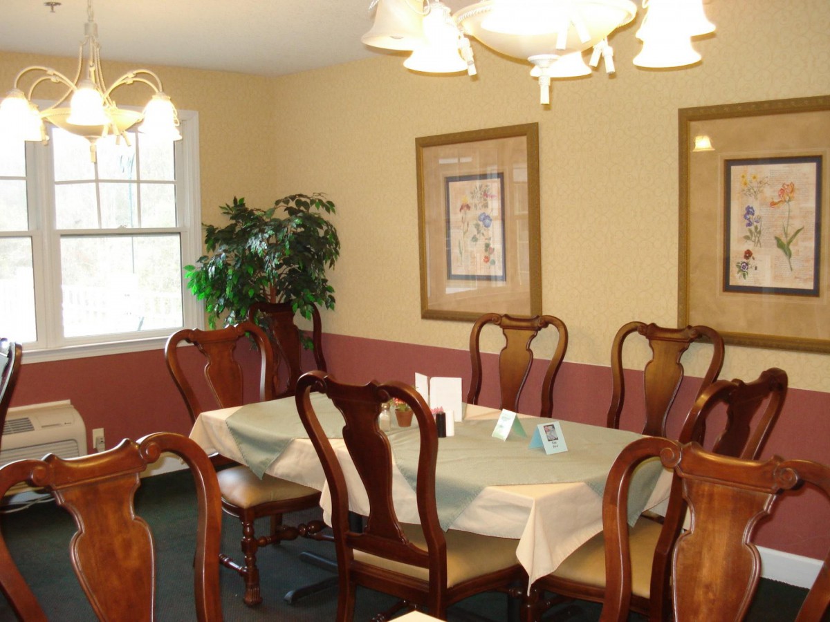 A cozy dining room featuring a large table with wooden chairs, elegant lighting, wall art, and a potted plant near the window.