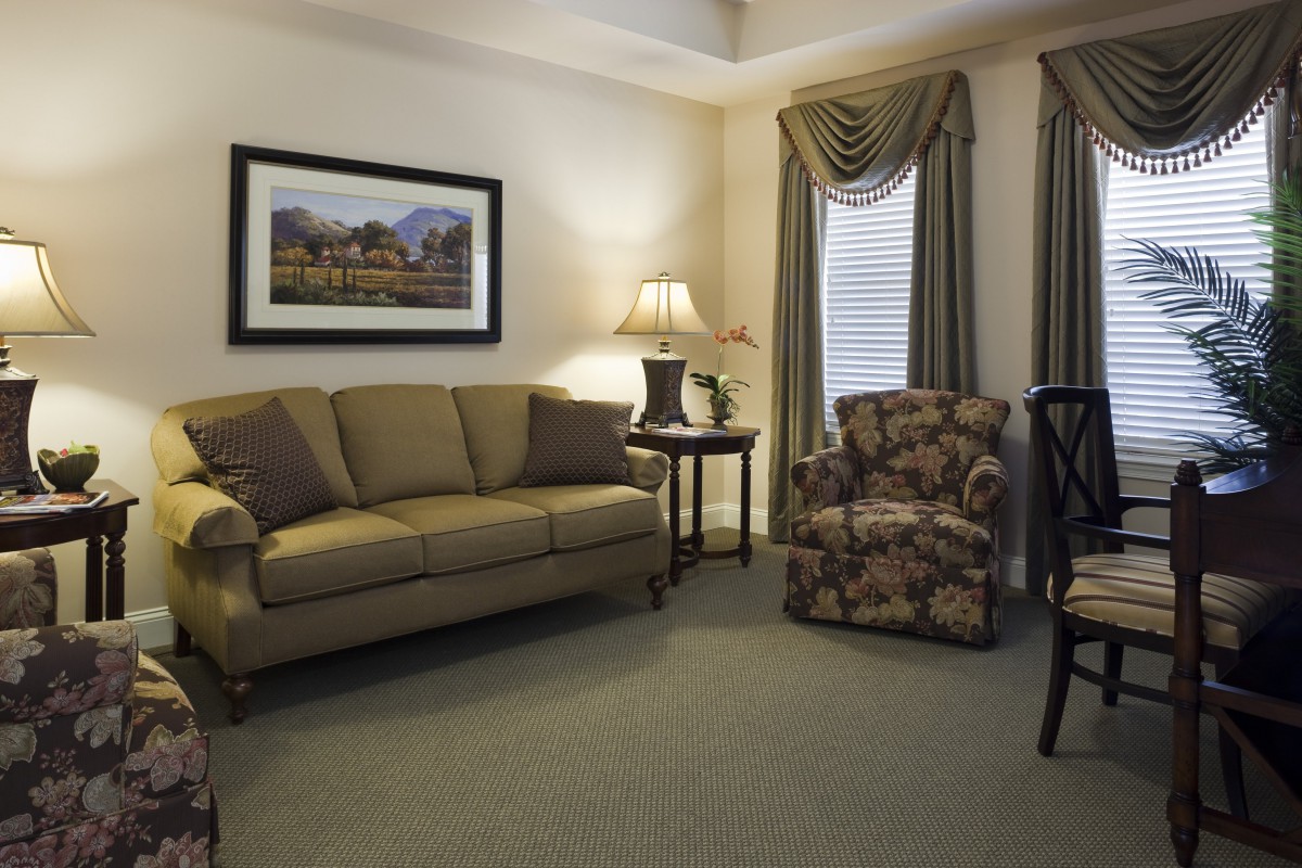 A cozy living room with traditional decor, featuring a beige sofa, floral armchair, and elegant curtains.