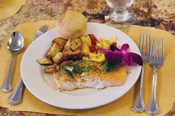 A delicious meal featuring salmon, roasted vegetables, and a roll on a elegantly set table.