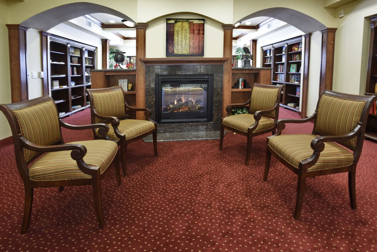 A cozy library seating area with four chairs surrounding a fireplace.