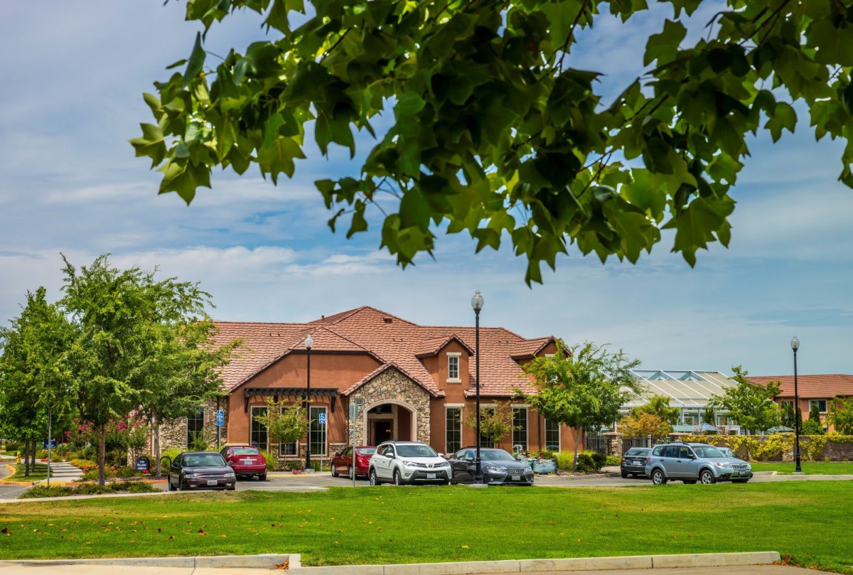 A suburban building with a parking lot, surrounded by trees and under a cloudy sky.
