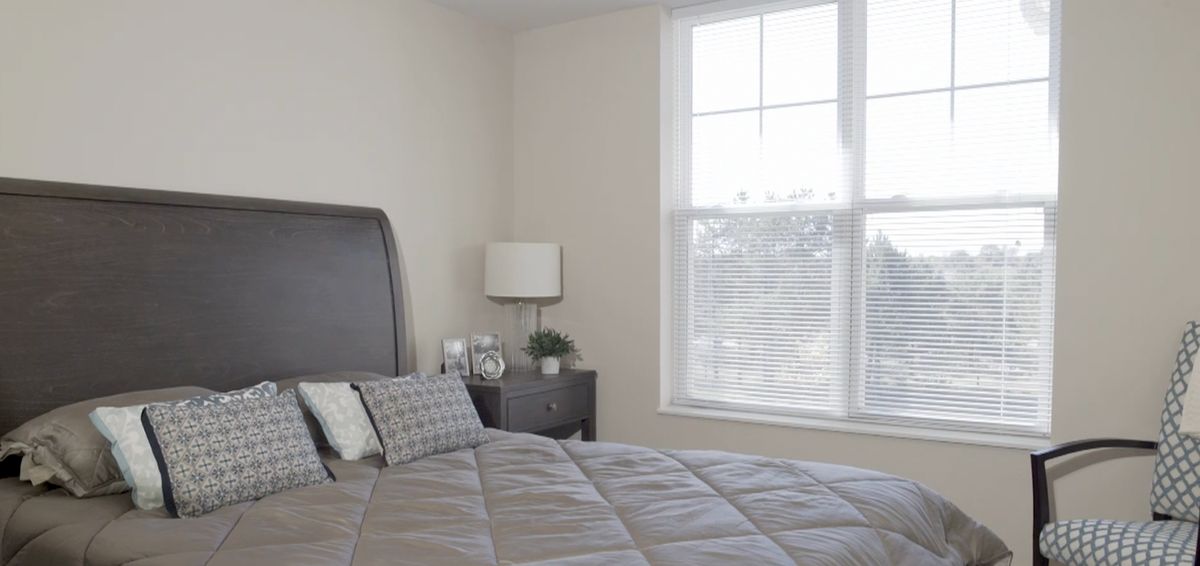 A minimalist bedroom with a neatly made bed, bedside table, and a large window.