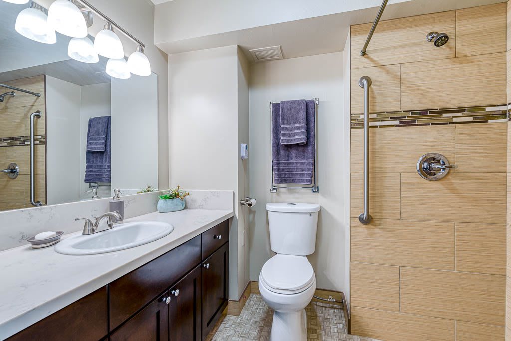 A modern bathroom with a large mirror, sink, toilet, and a walk-in shower.