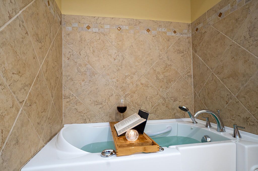A relaxing bathtub setup with a book and a glass of wine on a wooden tray.