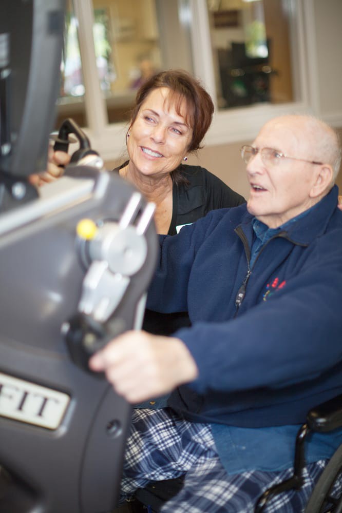 An elderly man exercising with the assistance of a trainer.