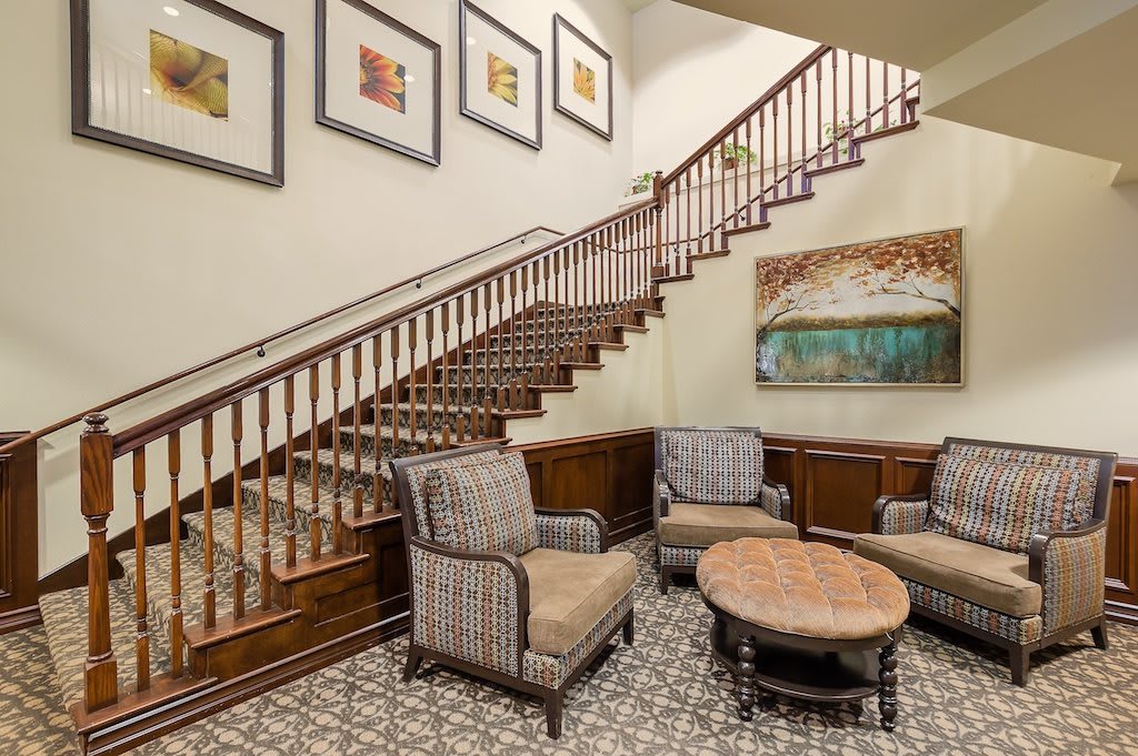 A cozy lobby featuring a wooden staircase, elegant seating area with patterned chairs, and wall artwork.