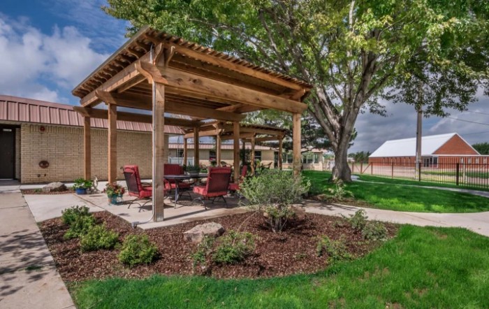 A picturesque outdoor area featuring a wooden pergola with seating, surrounded by a well-maintained garden and trees.