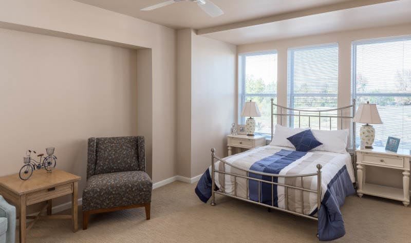 A cozy bedroom with a bed, chair, and large windows.