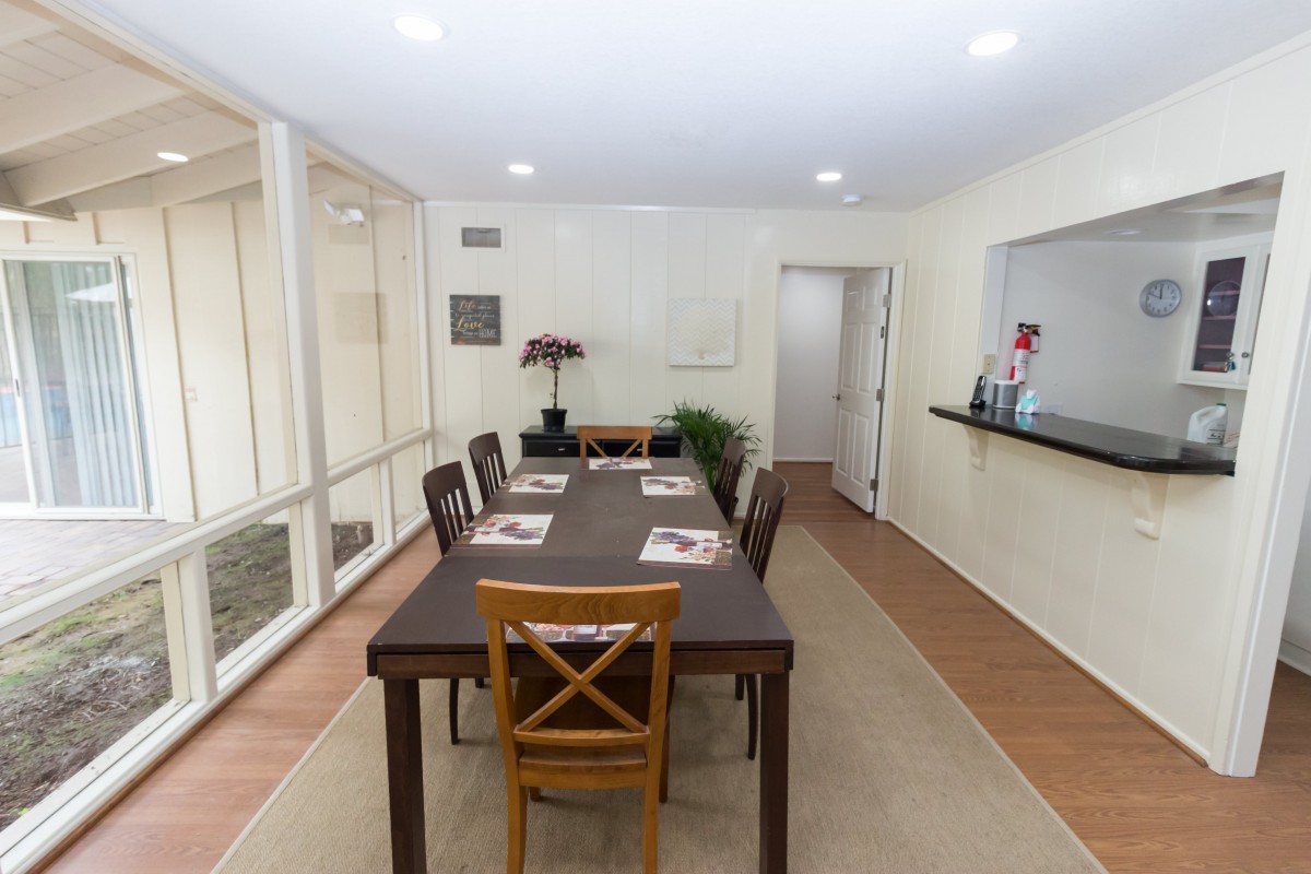 A modern dining room with a long table and chairs, featuring simple decor and warm lighting.