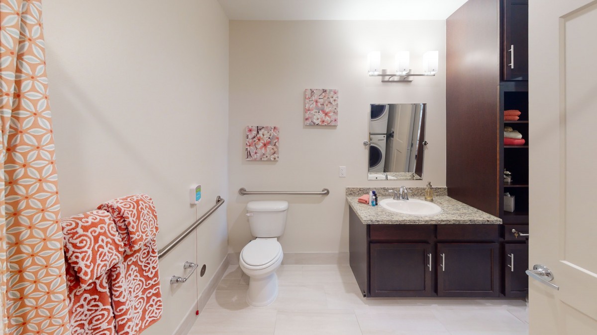 A clean and modern bathroom with accessibility features, including handrails and bright lighting.
