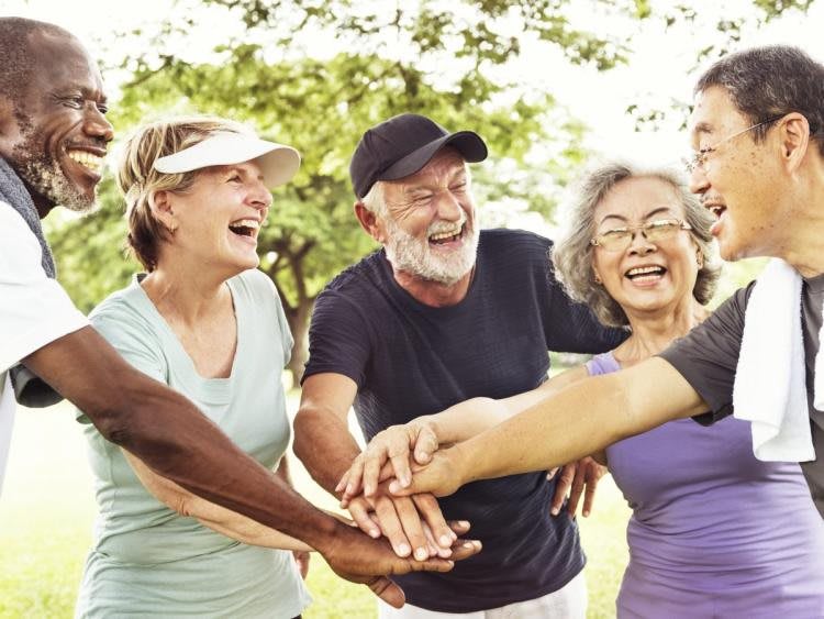 A group of friends smiling as they put their hands together outdoors, symbolizing teamwork and community.