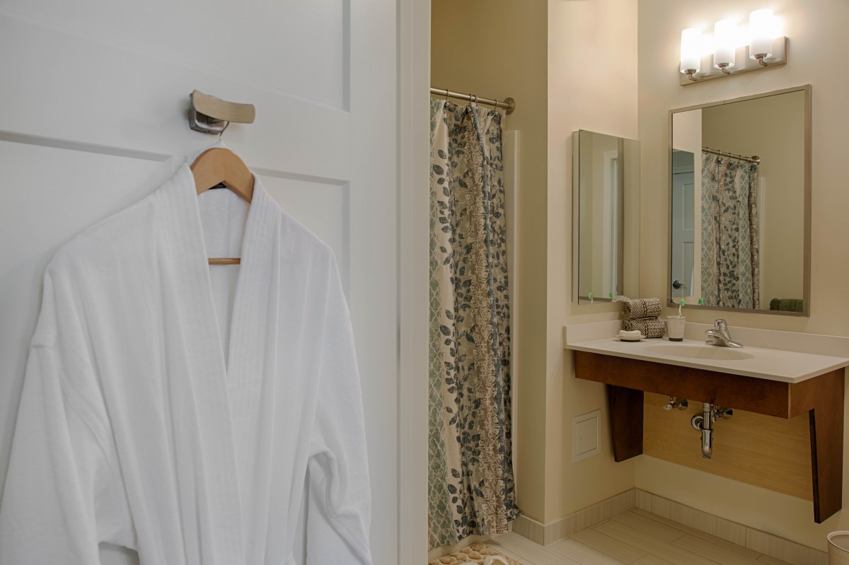 A cozy bathroom with a white robe hanging on the door and a shower in the background.